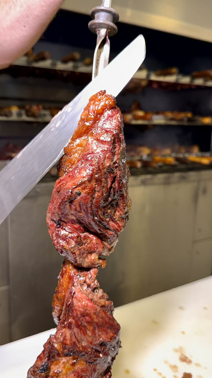 Carne assada sendo cortada na brasa
